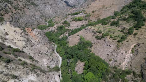 Aerial-flight-up-Gndevank-Canyon,-dirt-road-below-ancient-monastery