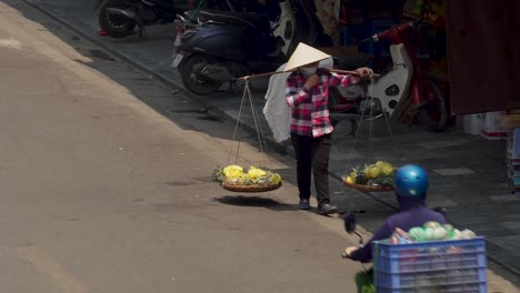 Mujer-Enmascarada-Vendiendo-Frutas-De-Una-Canasta-En-Las-Calles-De-Hanoi,-Vietnam.