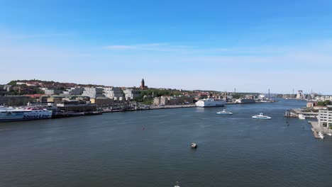 Vuelo-Aéreo-Con-Drones-Hacia-El-Río-Gota-Alv-Con-Ferries-Y-El-Paisaje-De-La-Ciudad-De-Gotemburgo-Al-Fondo-En-Un-Día-Soleado-En-Suecia