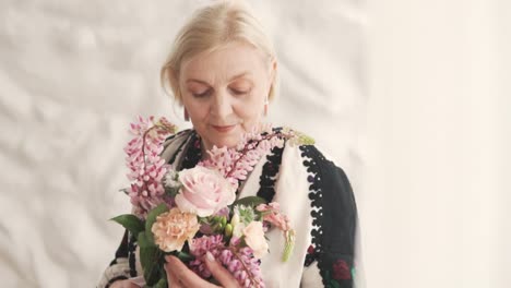 Das-Porträt-Zeigt-Eine-Hübsche-ältere-Grauhaarige-Frau-In-Authentischer-Bestickter-Ukrainischer-Kleidung,-Die-Einen-Wunderschönen-Blumenstrauß-Hält
