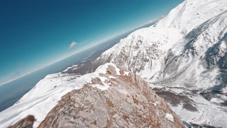 Dron-Fpv-Volando-Sobre-La-Cresta-De-Una-Montaña-Cubierta-De-Nieve-En-Un-Día-Claro