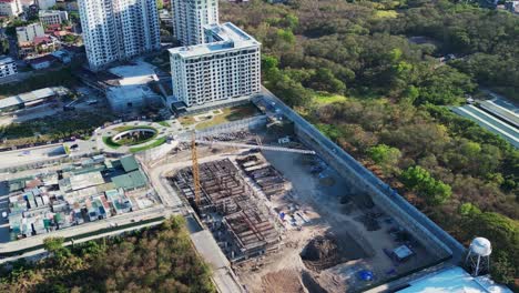 Aerial-overview-of-construction-site-grounds-and-crane-in-between-developing-cityscape-and-lush-greenery-of-Alabang,-Muntinlupa-City