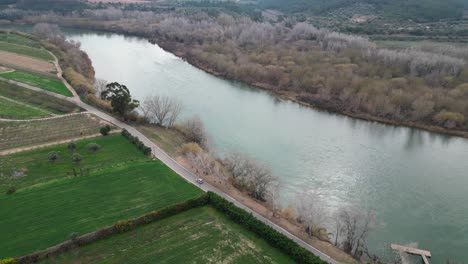 The-serene-ebro-river-winding-through-miravet-town-with-lush-greenery,-aerial-view