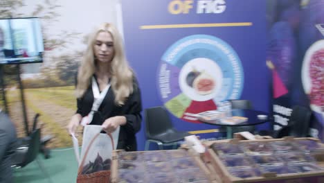 Female-employee-of-fig-company,-handing-branded-merchandise-at-food-trade-show,-Spain