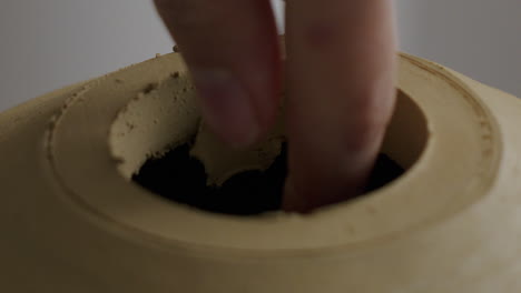 Close-up-shot-of-removing-clay-from-the-hole-of-a-pottered-vase-after-the-lid-was-removed-with-a-special-tool