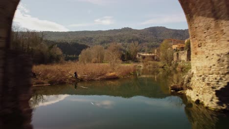 Ancient-stone-bridge-in-Besalu,-Spain,-reflecting-in-calm-river-on-a-sunny-day