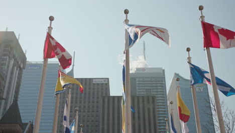 Flags-wave-infront-of-the-financial-district-on-a-bright-and-sunny-day-in-Toronto,-Canada