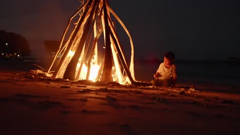 Junge-Spielt-Mit-Ast-Am-Lagerfeuer-In-Der-Tropischen-Nacht-Des-Komodo-Indonesien-Feuers,-Das-Im-Dunkeln-Brennt