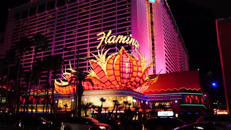 Flamingo-Casino-Hotel-and-Las-Vegas-Strip-Traffic-at-Night,-Vibrant-Light-on-Famous-Logo-and-Cars