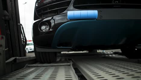 Close-up-of-a-black-car-loaded-on-a-tow-truck-in-a-parking-lot,-daylight