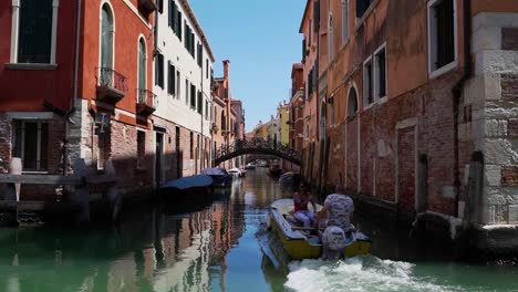 Boat-goes-around-the-curve-through-canal-in-Venice-towards-a-bridge