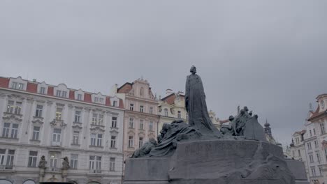 Toma-Panorámica-Sobre-El-Monumento-A-Jan-Hus-En-Praga-Bajo-Un-Cielo-Nublado,-Capturando-La-Arquitectura-Histórica