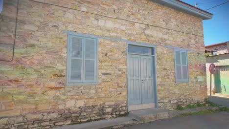 Steinhaus-Mit-Blauen-Fensterläden-Und-Einer-Passenden-Tür,-Vor-Einem-Strahlend-Blauen-Himmel