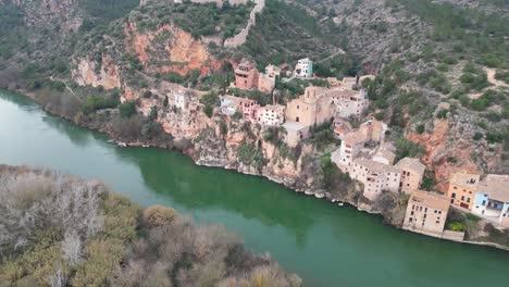 Miravet-town-in-tarragona,-spain-along-the-scenic-river-and-lush-landscape,-aerial-view