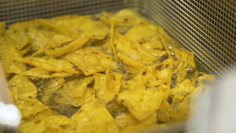 Tortilla-chips-in-frying-oil,-sizzling-nacho-crisps-in-hot-oil,-slow-motion