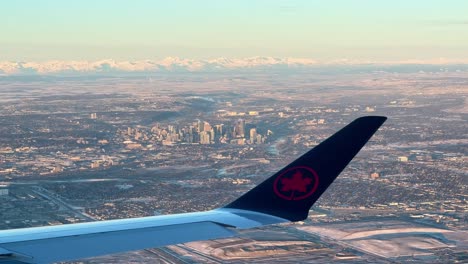 Looking-out-plane-window-at-plane-wing-with-Air-Canada-logo,-overlooking-city-of-Calgary-and-Rocky-mountains