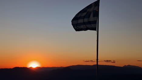 Greek-flag-blowing-in-the-wind-over-the-mountain-countryside-at-sunset