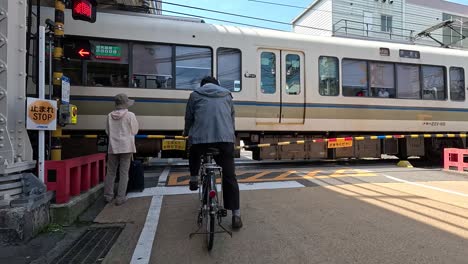 Mann-Auf-Fahrrad-Und-Fußgänger-Hielten-An-Und-Warteten,-Als-Züge-Auf-Der-Bahnstrecke-In-Japan-Kreuzten