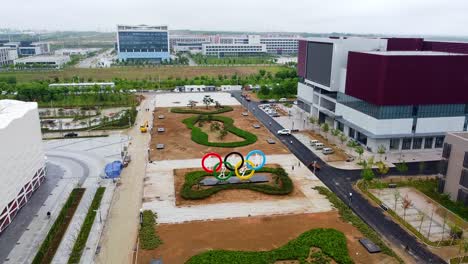 Aerial-ascending-shot-of-Olympics-logo-with-five-ring-symbol-of-the-Olympic-Games-in-Weihai-Olympic-Center,-Nanhai-New-District,-China-at-daytime