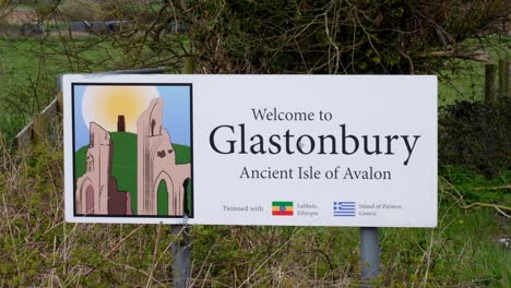 Welcome-to-Glastonbury-town,-the-ancient-isle-of-Avalon-sign-with-tourism-attractions-of-The-Tor-and-Abbey-in-Somerset,-England-UK