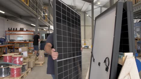 Men-loading-large-solar-panels-on-a-crate-for-shipping-at-Allo-Solar,-Handheld-dolly-left-follow-shot