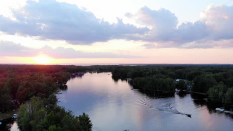 Rising-drone-shot-of-sunset-over-a-small-lake-in-Michigan-during-summertime
