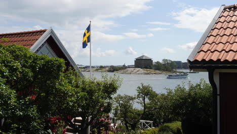 Schwedische-Flagge-Am-Ferienhaus-Mit-Boot-Im-Hintergrund,-Schweden