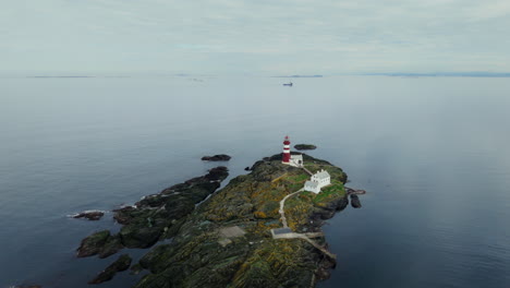 Aerial-establishing-shot-of-a-red-and-white-striped-lighthouse-in-Norway