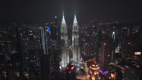 Panoramic-drone-shot-orbiting-the-night-lit-Petronas-Twin-Towers,-in-Kuala-Lumpur