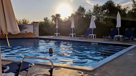Frau-Schwimmt-Im-Pool-Eines-Griechischen-Resorts-Mit-Goldenem-Sonnenlicht