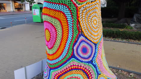 Colorful-crochet-knit-on-tree-trunk-in-Kyiv-city-Ukraine,-creative-street-art-graffiti-knitting,-4K-shot