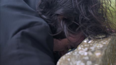 Crying-man-mourning-over-death-of-loved-one-at-grave-tombstone-in-cemetery