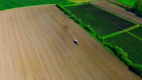 Luftaufnahme-Eines-Traktors,-Der-Ausgedehnte-Ackerflächen-Mit-Leuchtend-Grüner-Vegetation-Und-Sonnenkollektoren-Bestellt