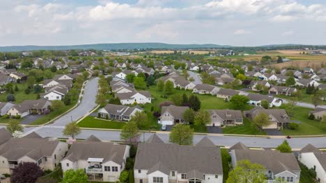 Sprawling-suburban-neighborhood-with-lush-green-lawns-and-winding-streets,-bordered-by-open-fields