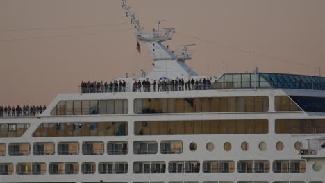 Passengers-Standing-Along-Top-Deck-Of-Cruise-Ship-During-Golden-Hour