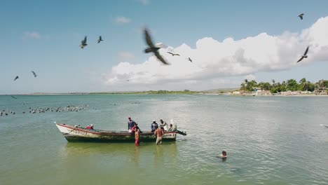 Viele-Pelikane-Und-Vögel-Fliegen-über-Ein-Fischerboot-Mit-Einer-Gruppe-Von-Männern,-Die-Tiere-Im-Wasser-Füttern
