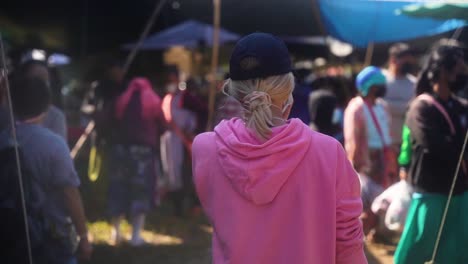 Eine-Blonde-Frau-Mit-Blauer-Mütze-Und-Rosa-Pullover-Trägt-Eine-Gesichtsmaske,-Als-Sie-An-Einem-Sommerabend-Auf-Einem-Lokalen-Markt-In-Thailand-Spazieren-Geht