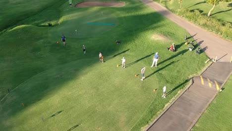 Golfista-Entrena-A-Algunos-Niños-En-Un-Impecable-Campo-De-Golf,-Niños-Practicando-Golpes-De-Salida