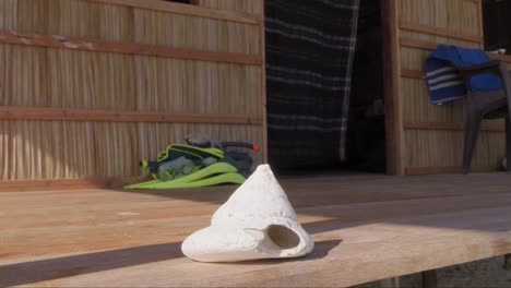 Close-up-of-a-seashell-on-a-wooden-deck,-with-snorkeling-gear-in-the-background,-set-in-a-rustic-hut-on-Kri-Island,-Raja-Ampat,-Indonesia