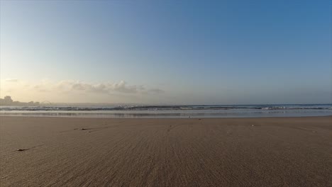 Steady-footage-of-the-beach-shoreline-sea-sand-with-calm-small-waves-crashing-in-the-back-below-a-sky-with-limited-clouds