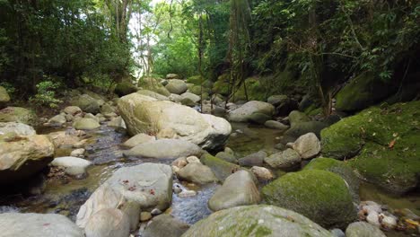 Un-Disparo-Bajo-De-Un-Dron-Pasando-Sobre-Grandes-Cantos-Rodados-Y-Rocas-Siguiendo-Un-Río-De-Agua-Dulce-Rodeado-De-árboles-En-Una-Selva-Tropical,-Santa-Marta,-Colombia