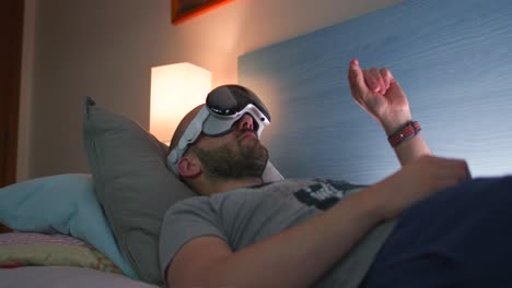 A-man-lies-on-bed-indoors-while-wearing-and-using-virtual-reality-VR-goggles