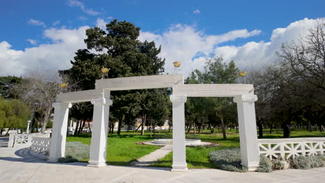 Ein-Eleganter-Weißer-Bogen-Mit-Säulen-In-Einem-öffentlichen-Park-In-Paphos,-Umgeben-Von-Grünem-Gras-Und-Bäumen