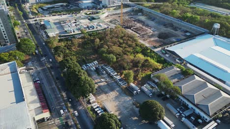 Aerial-drone-shot-of-cargo-trucks-parked-by-large-warehouse-and-construction-site-in-Alabang-City,-Muntinlupa,-Philippines