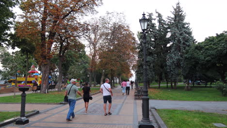 Menschen,-Die-In-Einem-Wunderschönen-Naturpark-Mit-Kinderspielplatz-Im-Stadtzentrum-Von-Kiew,-Ukraine,-Spazieren-Gehen,-Grünes-Gras-Und-Bäume,-4k-Aufnahme