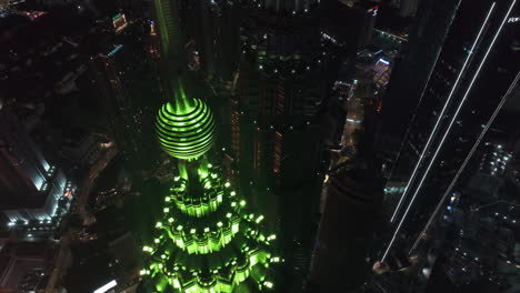 Drone-flying-over-the-illuminated-Petronas-Twin-Towers,-nighttime-in-Kuala-Lumpur