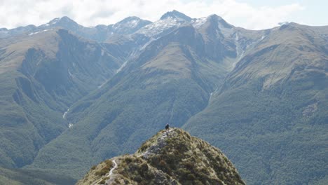 People-walking-through-a-moutain-range-with-mountains-behind-them-at-the-Brewster-Track-in-Mount-Aspiring-National-Park,-New-Zealand