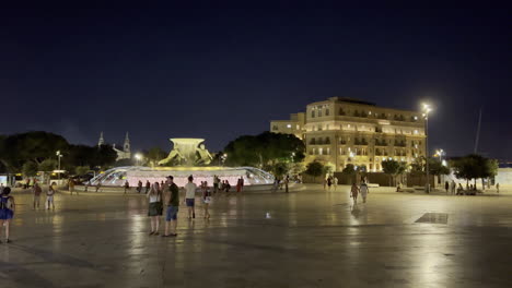 Triton-Fountain-Plaza-Vor-Dem-Stadttor-In-Der-Nacht,-Während-Touristen-Herumlaufen