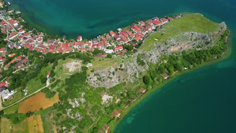 Península-De-Lin-Con-Casas-Con-Techos-Rojos-Junto-Al-Lago-Esmeralda,-Pogradec:-Un-Lugar-Ideal-Para-Unas-Vacaciones-Tranquilas,-Vista-Aérea