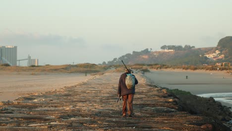 Lonely-fisherman-walking-on-a-sea-breakwater-at-sunset